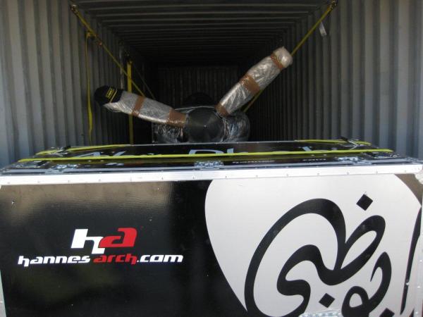A plane packed inside a shipping container with straps and padding for secure transport, featuring the logo of "hannesarch.com" on the container wall.